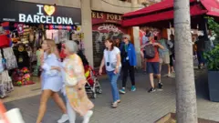 Pessoas caminhandoblaze apostas democalçada, com loja chamada 'I love Barcelona' atrás