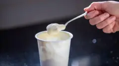 Foto de um pote branco de iogurte, com uma colher