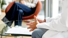 Bir doktor bir hastasıyla oturuyor ve konuşuyor. Göğüs aşağısını görüyoruz.