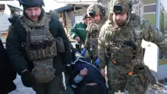 Люди в бронежелетах несуть на ношах ймовірно поранену людину на вулиці