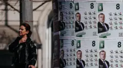 Женщина в Софии идет мимо расклеенных предвыборных плакатов в апреле 2026 года