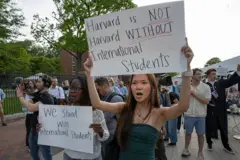 People holding up signs during a rally at the Harvard University campus. One of the signs says 'We stand with international students'.