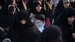 Mulheres vestidas com véus pretos seguram uma imagem do líder supremo do Irã, o aiatolá Ali Khamenei.