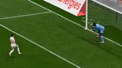 Futbolcu penaltıyı yeni kullanmış top havada gidiyor, Kaleci olduğu yerde topun kucağına gelmesini bekliyor.