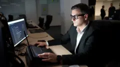 Ein Mann mit Brille sitzt in einer Cyber-Einsatzzentrale vor einem Computer.
