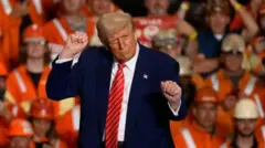 Trump gesticula frente a un grupo de obreros en una fábrica.