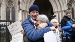 Сторонники Palestine Action обнимают друг друга и держат плакаты, празднуя победу в судебном разбирательстве против решения о запрете группы в соответствии с антитеррористическим законодательством, возле Королевского суда в Лондоне, Великобритания, 13 февраля 2026 года.