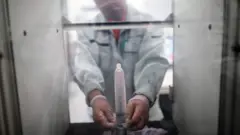 An employee of Japanese condom maker Sagami Rubber Industries puts a condom in a machine to test its endurance by filling it with air