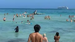 Beach goers swim towards the crashed helicopter