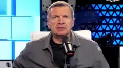 O apresentador de TV russo Vladimir Solovyov aparece olhando para a câmera, diante de um microfone, no estúdio de seu programa, Solovyov Live