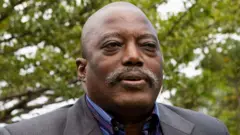 Joseph Kabila naa ree to ya fọto niwaju igi kan, o wọ aṣọ oyinbo alawọ eeru, o si wọ omin-in to ni awọ omi aro ati ila tẹẹrẹ sinu.