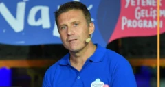 Mavi polo yaka tişört giymiş, renkli gözlü kumral bir erkek, mikrofon kulağına takılmış bir şekilde bir yer bakıyor.