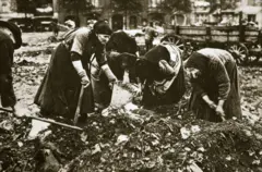 Un grupo de mujeres con cubos y azadas agachadas sobre un montón de basura en una foto de época.