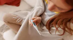 Joven con un termómetro en la mano.