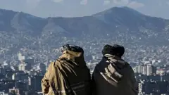 Dois membros do Talebã de costas para a câmera no topo de uma colina com vista para Cabul.