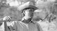 César Chávez segurando uma pá nos ombros enquanto trabalhava em horta comunitária em La Paz, na Califórnia, em 1975