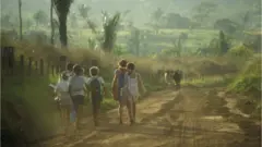 Crianças com material escolar caminham em estrada de terra