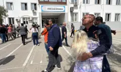 Saldırının yaşandığı okulun önünde toplanan aileler birbirlerine sarılarak destek veriyor. Arkada okulun ismi var.