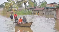 Abantu bari mu bwato, n'umugore inyuma arimo kwinjira mu nzu iri mu mazi