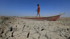 صبي يمشي على قارب على أرض جافة في أهوار الجبايش جنوبي العراق (يونيو/حزيران 2022)