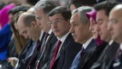 Arınç ve Davutoğlu yan yana oturuyor. Yanlarında çok sayıda siyasetçi daha var. Herkes ileri bakıyor, fotoğraf yandan çekilmiş