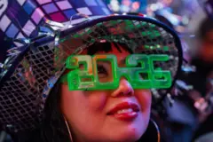 အမေရိကန်ပြည်ထောင်စု နယူးယောက်မြို့က နှစ်သစ်ကူးပွဲမှာမြင်တွေ့ရတဲ့ အမျိုးသမီးတစ်ဦး ၂၀၂၆ လို့ ရေးထားတဲ့အပျော်တမ်း အစိမ်းရောင် မျက်မှန်တပ်ထား 