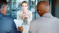 Mulher sendo entrevistada por dois homens para vaga de emprego