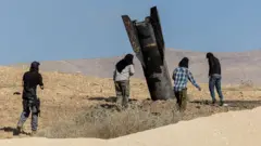 Parte de un misil lanzado sobresale del suelo en la zona de Cisjordania ocupada por Israel. Varias personas lo observan de cerca.