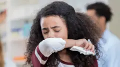 አፏን ሸፍና የምታስል ሴት