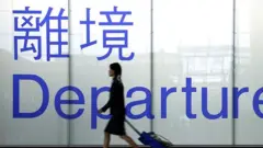 An airline steward in front of a departure gate sign in Chek Lap Kok airport, Hong Kong, 2003