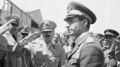 O xá Mohamed Reza Pahlavi e vários militares. Eles batem continência a ele.