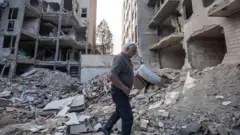 Um homem mais velho andando por destroços de prédios destruídos