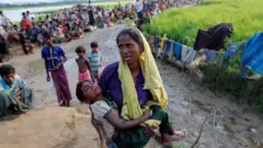 A Rohingya refugee woman who crossed the border from Myanmar a day before, carries her daughter and searches for help as they wait to receive permission from the Bangladeshi army to continue their way to the refugee camps, in Palang Khali, Bangladesh October 17, 2017.