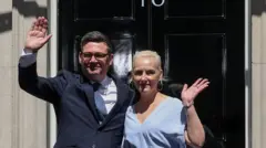 Nowo mianowany premier Wielkiej Brytanii, Andy Burnham, stoi przed siedzibą przy Downing Street 10 tuż po objęciu urzędu, machając zebranym. U jego boku stoi żona, Marie-France van Heel. Londyn, Wielka Brytania, 20 lipca 2026 r. Źródło: Reuters/Isabel Infantes.