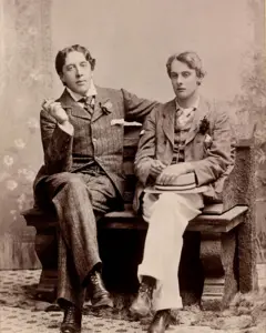 O escritor irlandês Oscar Wilde (1854-1900), retratado em 1893 com seu amante, Alfred Douglas (1870-1945), ambos de terno, sentados