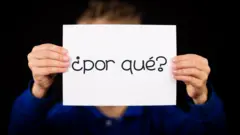 Una persona sosteniendo un cartel con la pregunta ¿por qué?