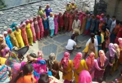 Decenas de mujeres y algunos hombres de la comunidad hatti, vestidos con ropas coloridas, forman un círculo alrededor de dos hombres que tocan tambores.