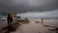 Pessoas na praia com nuvens escuras ao fundo.