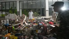 Pessoas em meio a uma cena caótica de destroços no refeitório dos médicos após o acidente. Está claramente escuro lá fora, o que significa que já se passaram várias horas desde o incidente