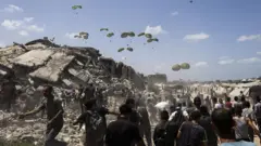 Aviões lançam pacotes de ajuda humanitária por paraquedas enquanto palestinos se aglomeram na área onde os pacotes caem, a oeste da cidade de Gaza.