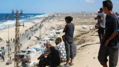 يشاهد فلسطينيون أشخاصاً يصلون مع ممتلكاتهم على طريق ساحلي شمال غرب مخيم النصيرات للاجئين، أثناء نزوحهم جنوباً من وادي غزة.
