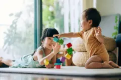 Dois irmãos brincando de montar blocos no chão de uma sala