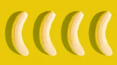 Sarı bir arka plan üzerinde yan yana dizilmiş, kabukları soyulmuş dört muz.