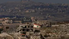 رُسم علم لبناني على مبنى متضرر في قرية ميس الجبل جنوب لبنان، من موقع على الجانب الإسرائيلي من الحدود في 23 يناير/كانون الثاني 2025 في شمال إسرائيل. 