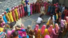 Dezenas de mulheres e alguns homens da comunidade hatti, vestidos com roupas coloridas, formam um círculo em volta de dois homens tocando tambores