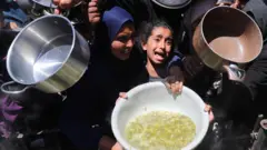 فتاة تبكي، بينما ينتظر فلسطينيون الحصول على طعام مطبوخ في مطبخ خيري، في بيت لاهيا، شمال قطاع غزة
