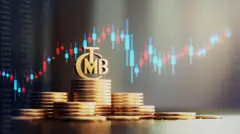 madeni paralar üst üste dizilmiş üzerinde TCMB amblemi var hepsi altın rengi ve arkada borsa işlemleri var mavi ve kırmızı bir grafik.