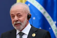 Lula falando, com equipamento de tradução no ouvido e bandeira do Brasil atrás
