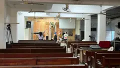 Preparação de igreja para culto, onde se vê bancos, telão e pessoas organizando encontro