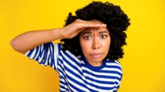 Uma mulher negra,casa de aposta com cassinocabelos cacheados vestindo camiseta listradacasa de aposta com cassinoazul e branco, com a mão direita sobre a testa 